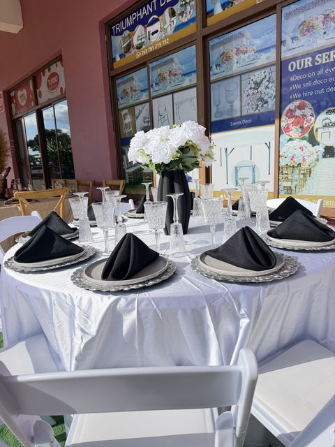 Round table with black napkins, silver chargers and a white floral centerpiece, by Triumphant Events