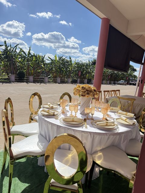 Gold oval-back chairs paired with a round table and floral centerpiece, set up outdoors