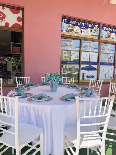 Round table styled with teal chargers and napkins, a gold vase centerpiece and white chiavari chairs, by Triumphant Events