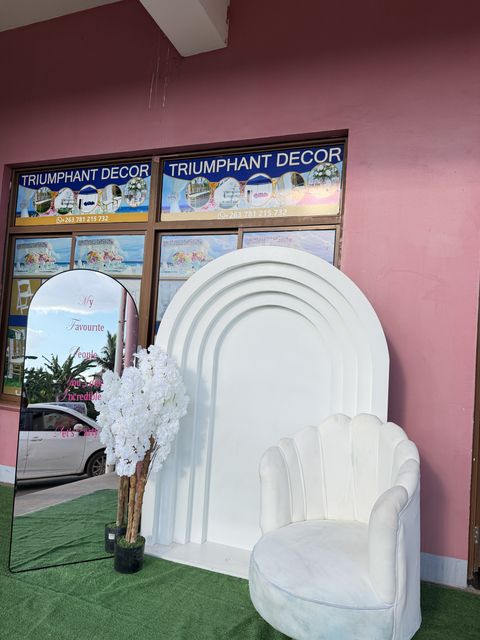 White arch backdrop with a round mirror and velvet chair, set up outdoors