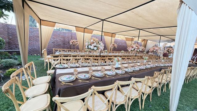 Wide view of a marquee tent reception with rattan cross-back chairs lining a long table, by Triumphant Events