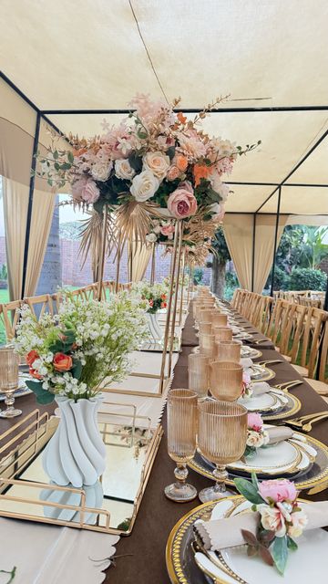 Close-up of a tall floral centerpiece and gold-rimmed place setting under a marquee tent